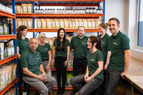 Das bioKontor Team vor dem Lagerregal mit Bio-Produkten wie Pulver, Kapseln und Ölen